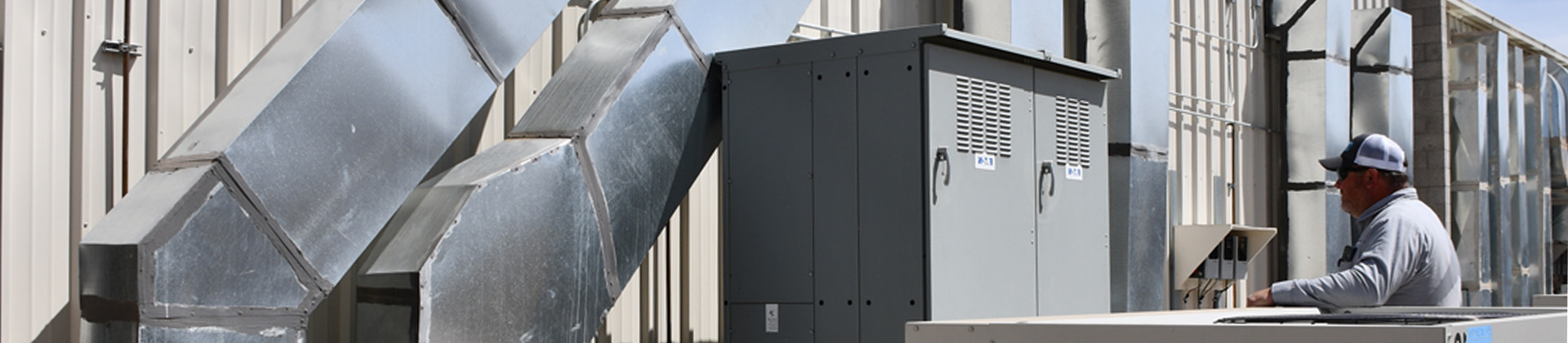 A GNS technician works beside a commercial unit and large ductwork.