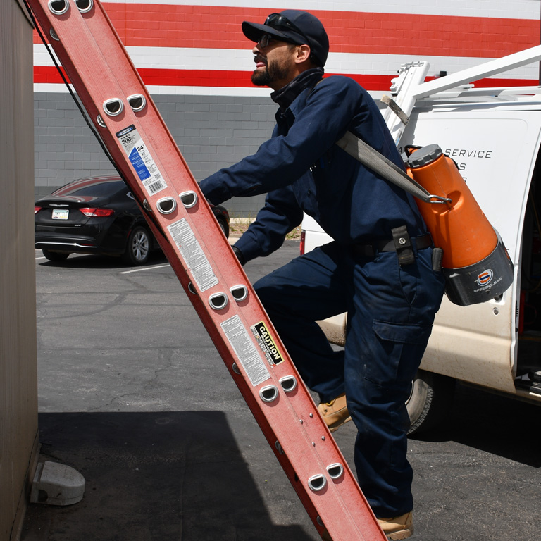 A GNS technician climbs a ladder to a rooftop unit.